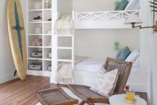 a surfer chic kids’ room with white and stained furniture, neutral and pastel bedding, a surfing board, built-in shelves and cool built-in bunk beds