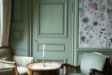 a vintage living room with floral wallpaper, green molding on the walls and door, chic vintage furniture, a round table and a cool artwork