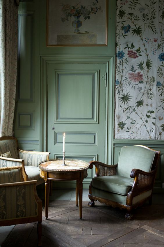 a vintage living room with floral wallpaper, green molding on the walls and door, chic vintage furniture, a round table and a cool artwork