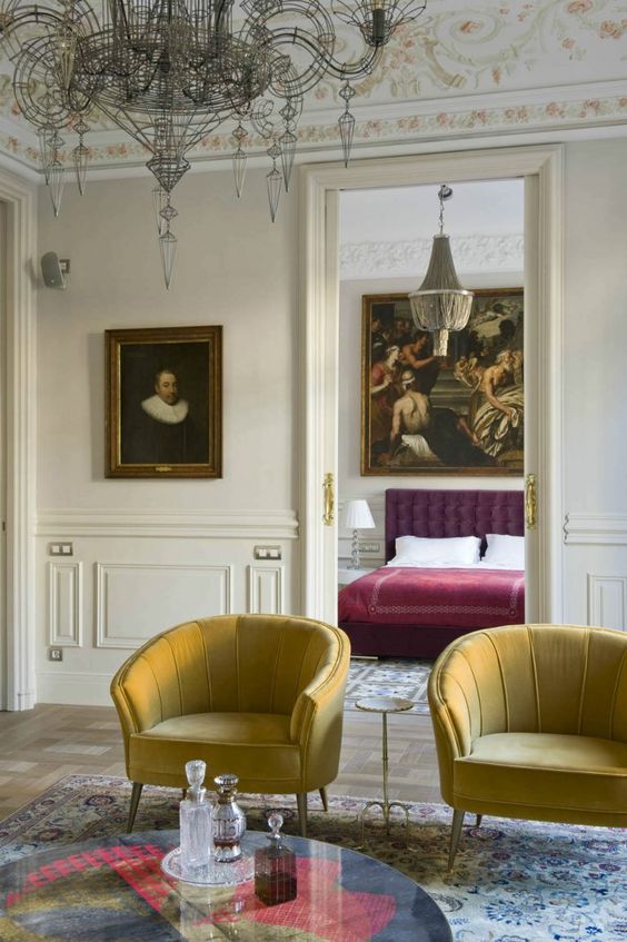 a vintage living room with paneling, yellow antique chairs, a printed rug and some artworks