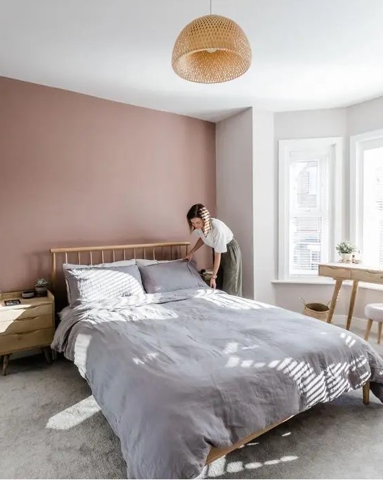 a welcoming and airy bedroom with a mauve accent wall, a wooden bed and wooden furniture, a rattan pendant lamp