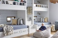 a welcoming beachfront grey kids’ room with four built-in bunk beds, grey and yellow bedding, cushions, pillows and beanbag chairs