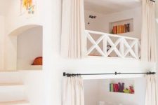 a white kids’ room with built-in bunk beds, shelves, bright bedding, built-in lights and lamps is a cool and welcoming space
