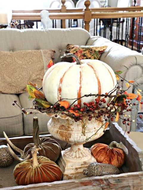 a white painted pumpkin with twigs and faux berries placed in a vintage urn as a stand for a shabby chic touch