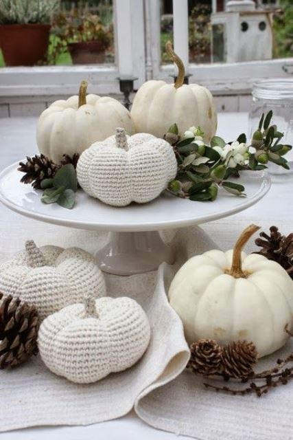 a white porcelain stand with greenery, berries, pinecones, natural and crochet white pumpkins