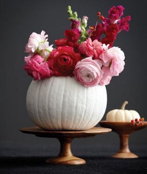 a white pumpkin on a wooden stand with red, fuchsia and pink blooms as a chic and bright fall centerpiece