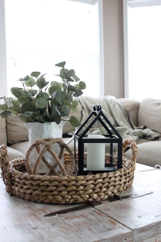 a whitewashed shabby chic coffee table with a woven tray, a candle lantern, a greenery arrangement in a white vase