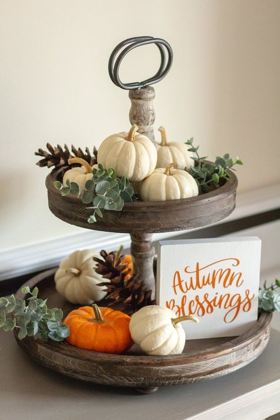a wooden tiered stand with natural pumpkins, pinecones, eucalyptus and a mini sign is a cool fall decoration