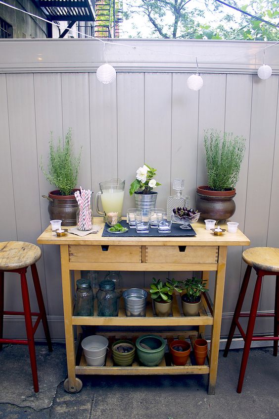 an IKEA Forhoja cart used as a storage piece for outdoors and an outdoor bar with potted greenery and soem lemonade