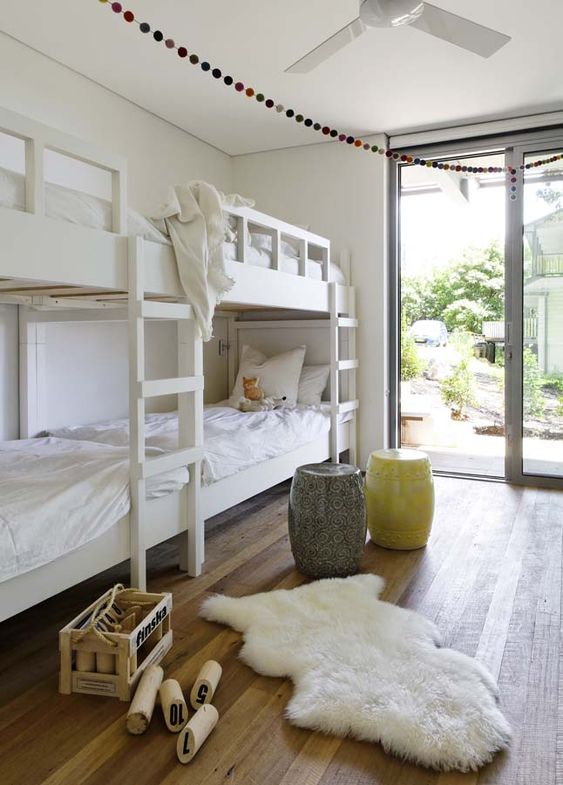 an airy kids' bedroom with built-in bunk beds with white bedding, a yellow and a grey side table and a faux fur rug