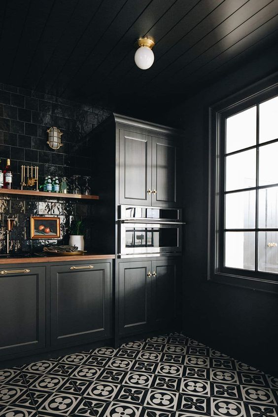 an elegant black kitchen with shaker cabinets, a glossy black tile backsplash, black and white printed tiles and butcherblock countertops