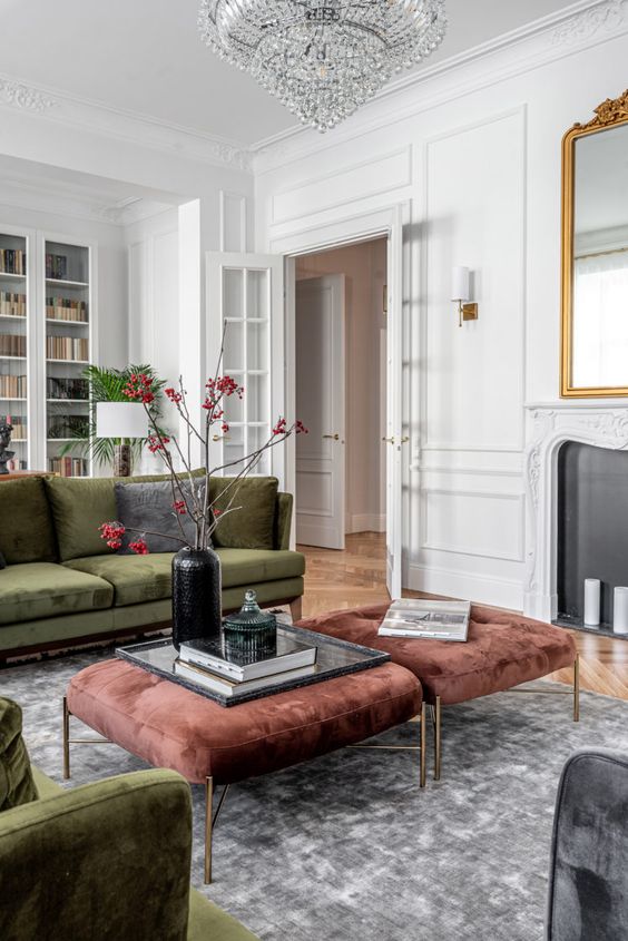 an exquisite living room with molding on the walls, green sofas and brown ottomans, a crystal chandelier and a non-working fireplace