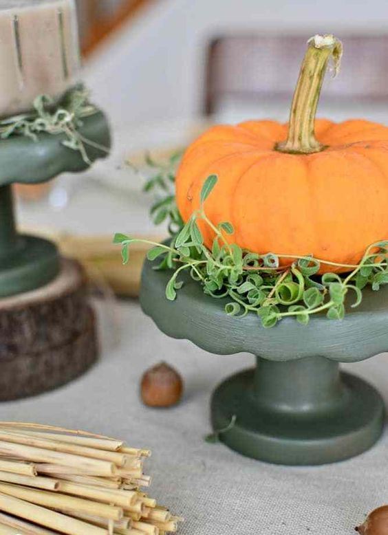 an orange pumpkin with greenery placed on a black stand is a bold and modern fall centerpiece