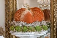 an orange velvet pumpkin, ha and moss balls on a vintage stone stand is a fun and playful fall decoration