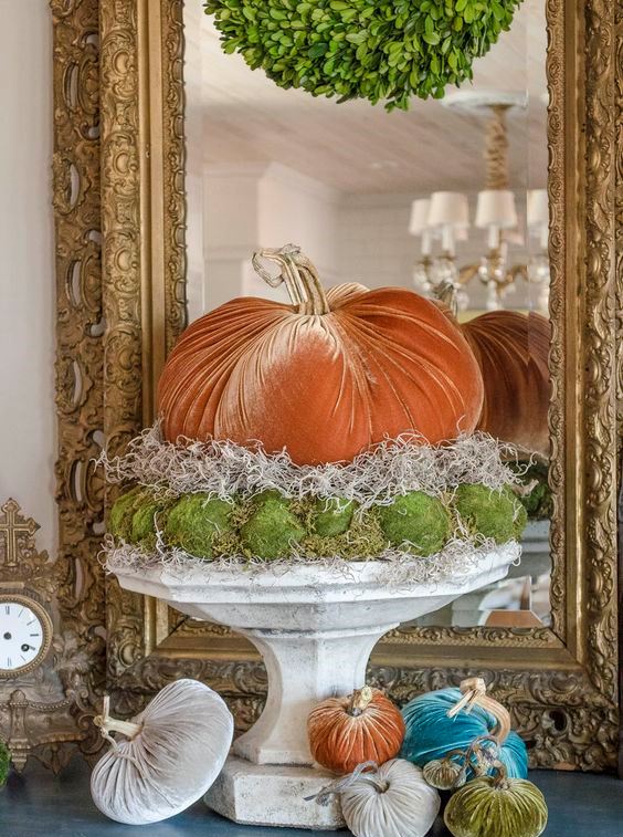 an orange velvet pumpkin, ha and moss balls on a vintage stone stand is a fun and playful fall decoration