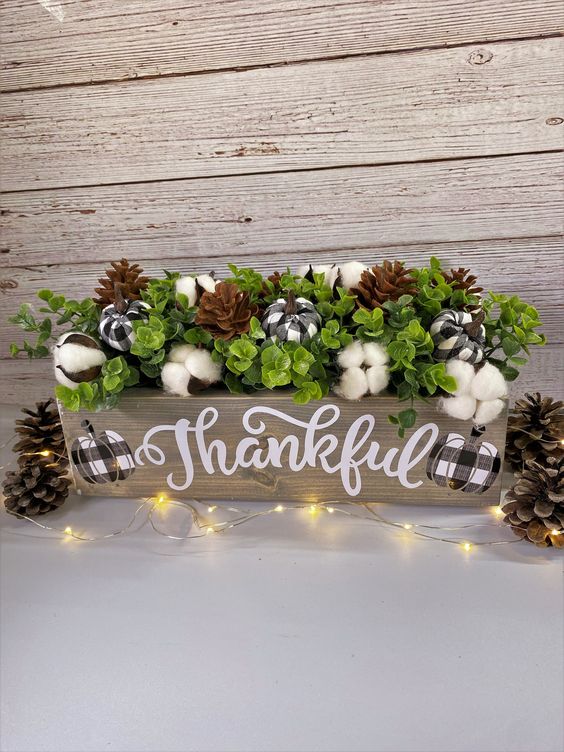 a Thanksgiving centerpiece of a wooden box, faux greenery, cotton, pinecones and mini plaid pumpkins is a lovely idea