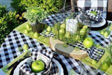 a Thanksgiving table setting with a buffalo plaid tablecloth, plates and napkins, a green table runner, greenery and green apples