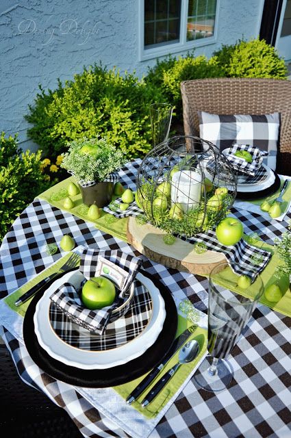 a Thanksgiving table setting with a buffalo plaid tablecloth, plates and napkins, a green table runner, greenery and green apples