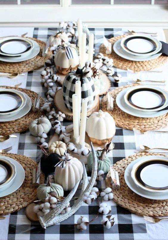 a Thanksgiving tablescape with a plaid tablecloth, woven mats antlers, cotton, pumpkins, candles and white and black porcelain