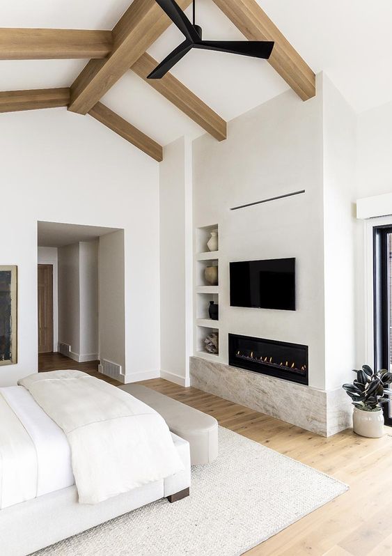 a beautiful and sleek creamy bedroom with wooden beams, a built-in fireplace, built-in shelves and potted plants