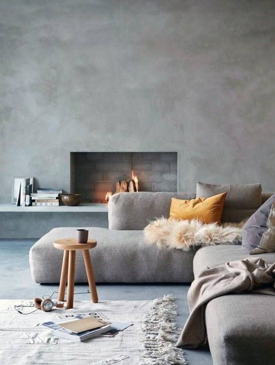 a beautiful minimalist living room with chic furniture, a concrete wall and a fireplace and cozy textiles