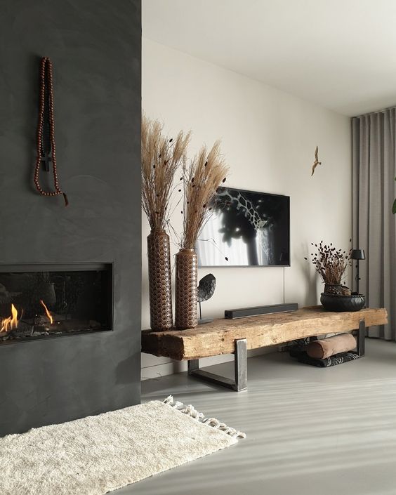 a boho monochromatic living room with a built-in fireplace, a rough wood bench, a TV on the wall and dried grass arrangements