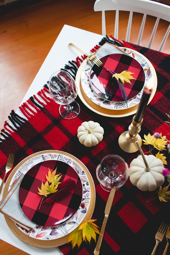 a bold Thanksgiving place setting with a gold charger, a floral and a plaid plate plus bold fall leaves on top