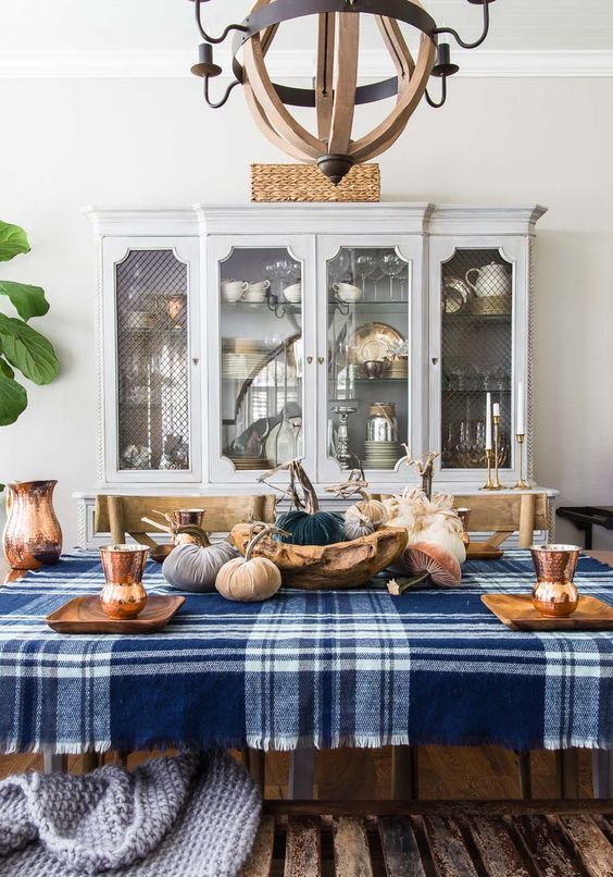 a bold Thanksgiving tablescape with a blue plaid tablecloth, a wooden bowl, velvet pumpkins, copper cups and wooden chargers