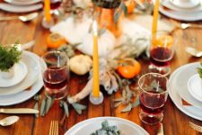 a bold modern Thanksgiving tablescape with bright blooms and candles, antlers, eucalyptus, white porcelain and rust napkins