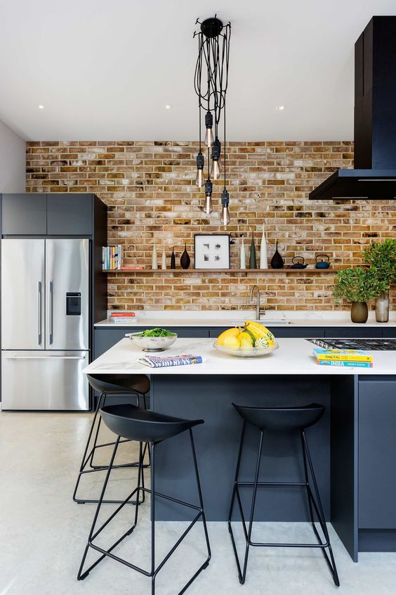 a bold modern kitchen with graphite grey lower cabinets, a brick wall, a black hood, a large kitchen island and black stools