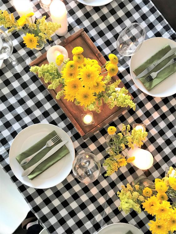 a bright Thanksgiving tablescape with a plaid tablecloth, grene napkins, bold yellow blooms and candles and cutlery
