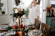 a chic Thanksgiving table setting with a plaid runner and napkins, bold blooms, black candles and wood slices