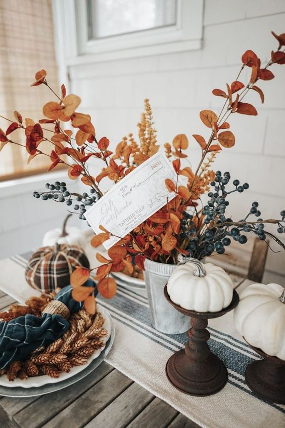 a chic Thanksgiving table setting with a striped runner, faux white pumpkins, leaves, berries, a plaid pumpkin and plaid napkins