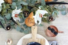 a chic modern Thanksgiving table with a greenery and white bloom runner, antlers, copper cutlery and mugs, wooden boards and agates