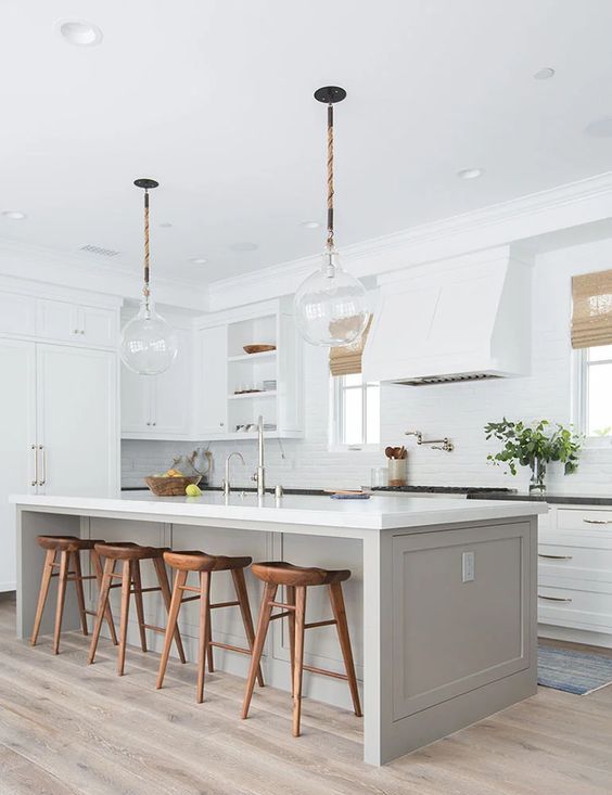 a chic modern farmhouse kitchen with white shaker style cabinets, a dove grye kitchen island, a large hood, rich-stained stools