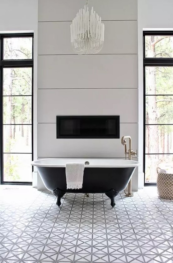 a chic vintage bathroom with white geo tiles, a black clawfoot bathtub, a built-in fireplace and a chic chandelier