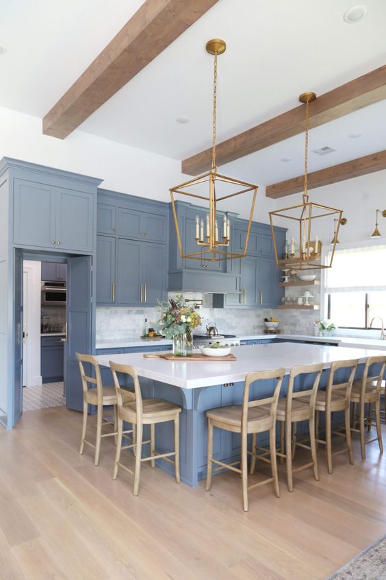 a coastal kitchen done in ocean blue, with a white marble tile backsplash, a large kitchen island and vintage pendant lamps