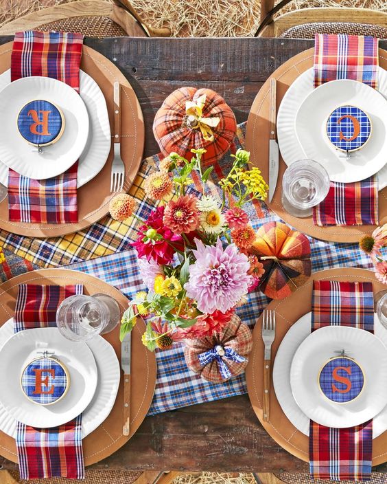 a colorful Thanksgiving tablescape with bright plaid table runners and napkins, plaid embroidery hoops, bright flowers and plaid pumpkins
