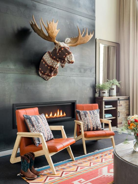 a contemporary fireplace nook with a concrete clad fireplace, a faux taxidermy piece, orange chairs and pillows plus cowboy boots