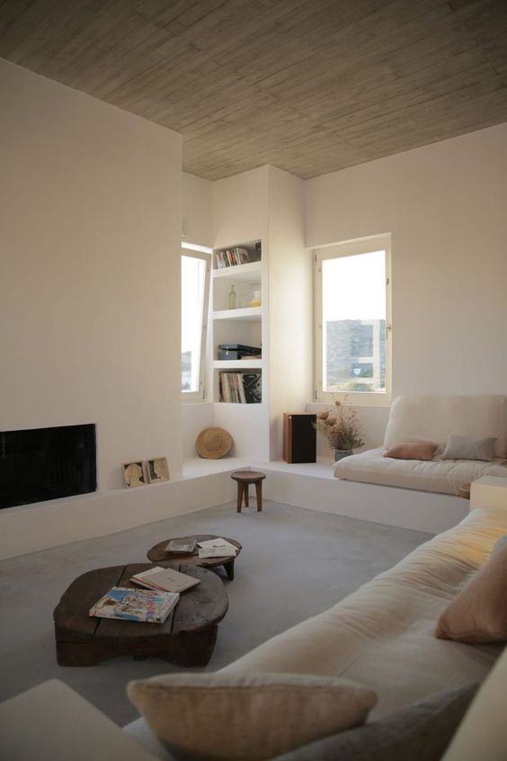 a contemporary neutral living room with a built-in fireplace a built-in sofa with neutral upholstery, built-in shelves and low coffee tables