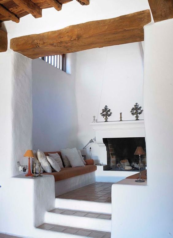 a conversation nook by the fireplace, with a brick clad fireplace, upholstered benches with lots of cushions and pillows