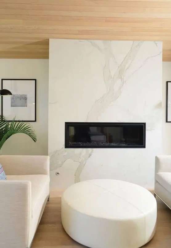 a cozy minimalist space with a white marble fireplace, neutral furniture and a wooden ceiling is very chic