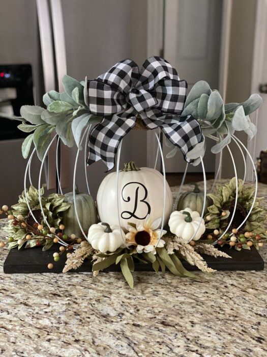 a creative Thanksgiving centerpiece of a wooden plaque, some faux pumpkins, a wire pumpkin with greenery and a plaid bow
