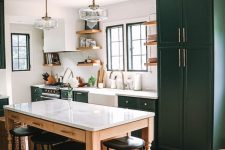 a dark green farmhouse kitchen with shaker style cabinets, a table that doubles as a kitchen island and black vintage stools