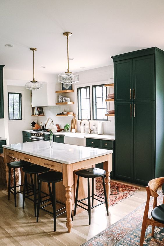 a dark green farmhouse kitchen with shaker style cabinets, a table that doubles as a kitchen island and black vintage stools