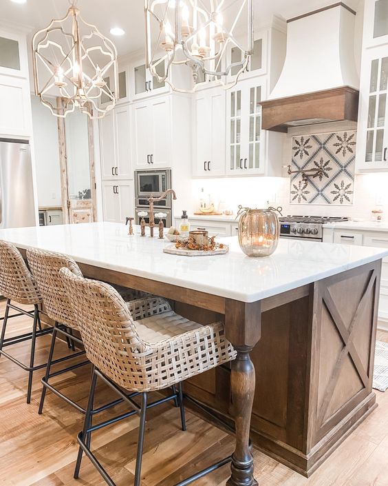 a fabulous vintage kitchen with white cabinets, a stained kitchen island with vintage legs, chic pendant lamps and woven stools