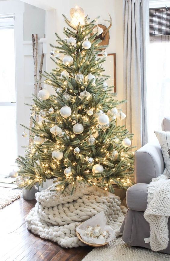 a fantastic Christmas tree with lights and white and silver ornaments plus a white chunky knit tree skirt is gorgeous