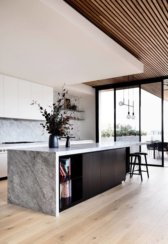 a fantastic minimalist kitchen with white cabinets, grey marble countertops and a backsplash, a black kitchen island with a waterfall countertop and black stools