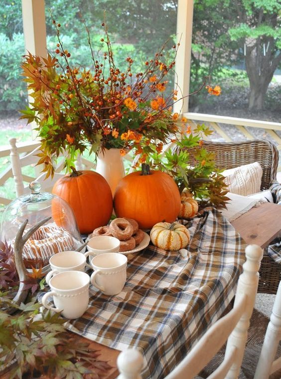 a farmhouse Thanksgiving tablescape with a plaid runner, leaves, pumpkins, greenery and berries in a vase and antlers