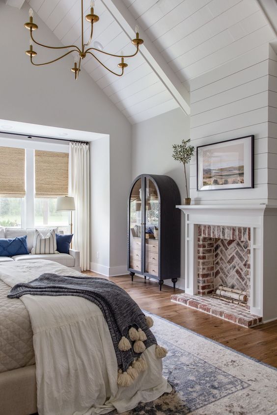 a farmhouse bedroom with planked walls and a ceiling, a fireplace, a bed with neutral bedding, a white sofa and a vintage bookcase